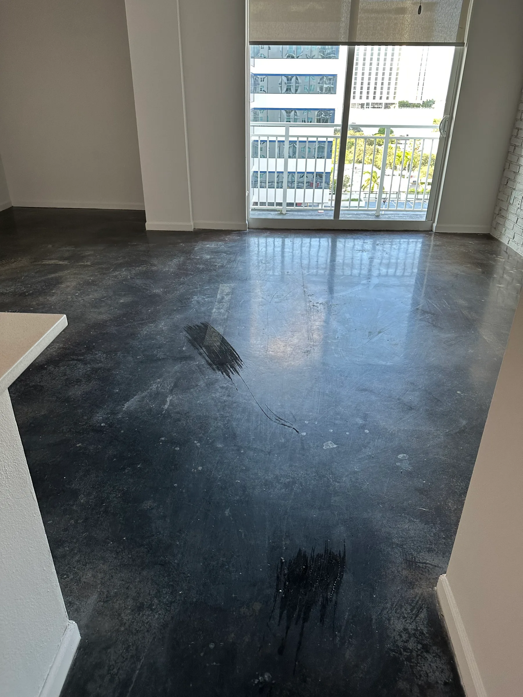 Empty room with dark polished concrete floor and glass doors overlooking urban balcony view.