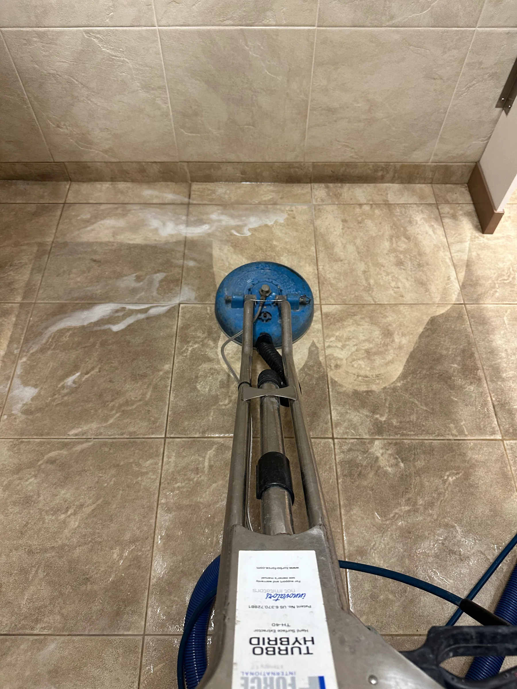 Professional tile floor cleaning machine with blue head on beige ceramic tile floor.